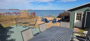 A patio with outdoor seating, a view of the sea, and a small building with a door.