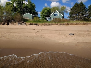 En sandstrand med fodaftryk, der fører hen til et grønt hus med et hvidt vindue.