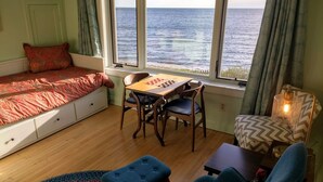 Une pièce confortable avec un lit, une table sur laquelle est posé un jeu de société, et une vue sur la mer.