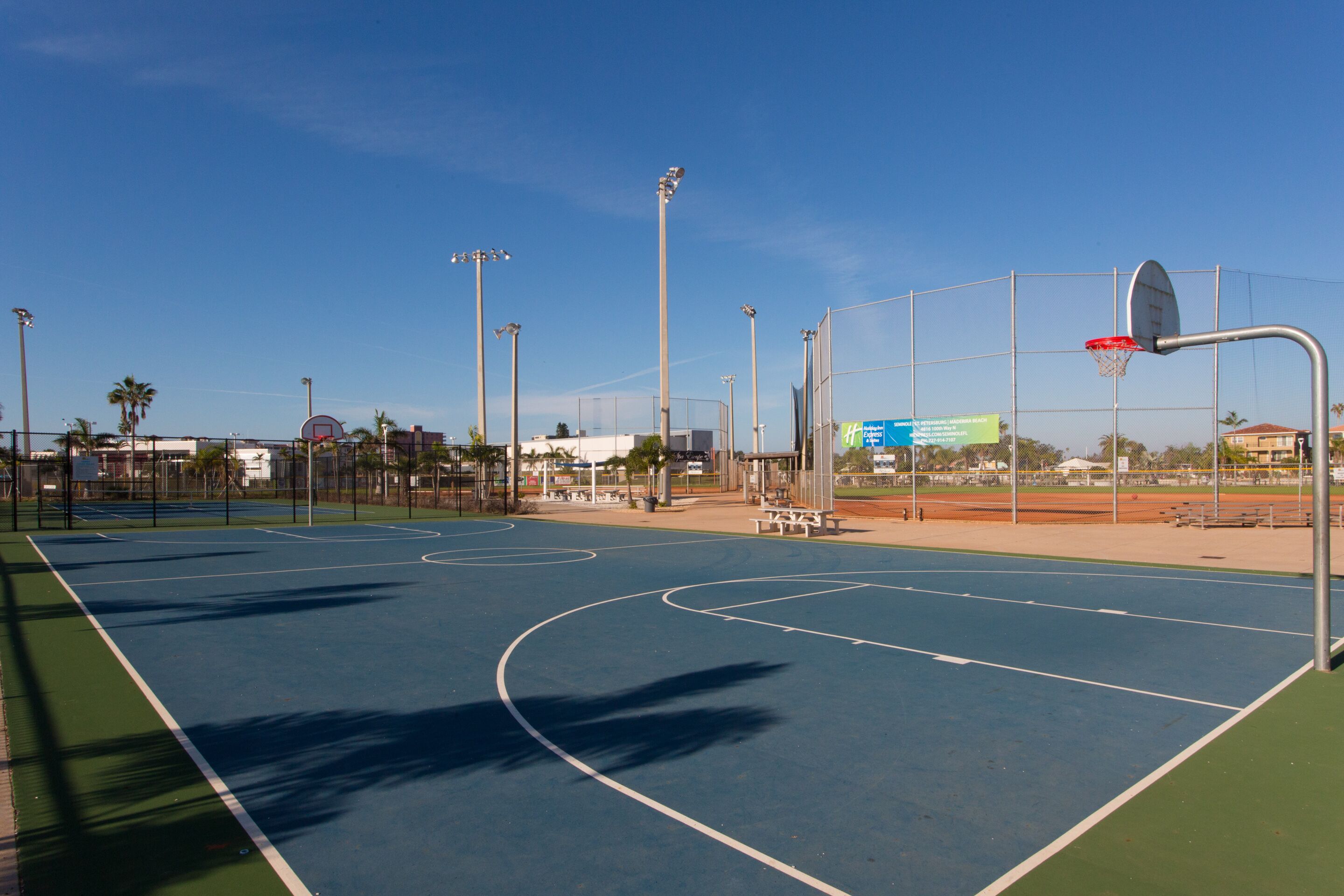 Un terrain de basket-ball extérieur avec des marquages bien visibles, un panier et une clôture périphérique.