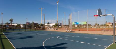 Un terrain de basket-ball extérieur avec des marquages bien visibles, un panier et une clôture périphérique.