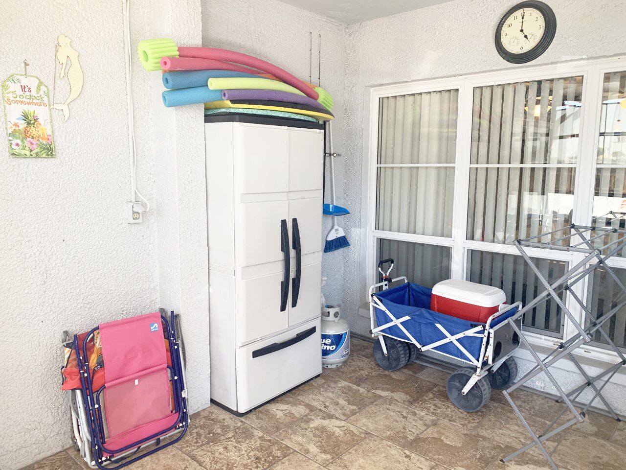 Una habitación con un armario blanco, un carrito azul con un refrigerador y una ventana con persianas.