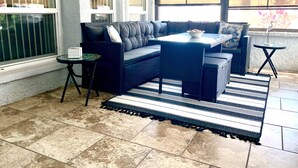 A sunlit patio area with a dark-colored sofa, a small round table, and a striped rug. - Come to your HAPPY PLACE! 2/2 ground floor waterfront community Condo! (Madeira Beach)