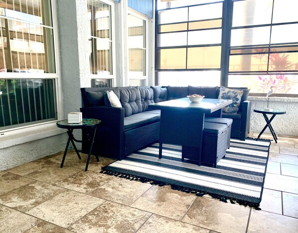 A sunlit patio area with a dark-colored sofa, a small round table, and a striped rug.
