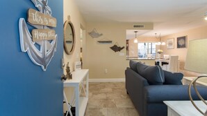 A living room with a blue couch, a white table, and decorative wall art including an anchor and a mirror. - Come to your HAPPY PLACE! 2/2 ground floor waterfront community Condo! (Madeira Beach)