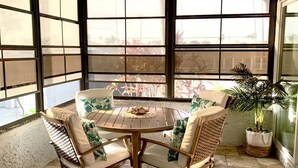 A round wooden table with four wicker chairs, each with a cushion. The room has large windows with a view of the outside. - Come to your HAPPY PLACE! 2/2 ground floor waterfront community Condo! (Madeira Beach)