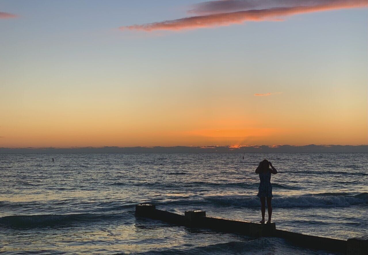 Una persona de pie en un muelle al atardecer, con el océano de fondo.