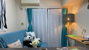 A room with a blue sofa, a panda plush toy, a table with a remote control, a lamp, and a window with teal curtains. - Today's Relaxing and Fun Studio! Near Olympic Park! (Setagaya)