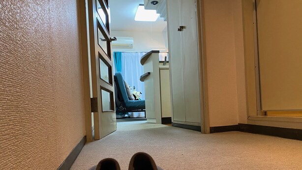 A hallway with a pair of slippers on the floor, a door leading to a room with a bed and a chair, and a wall-mounted air conditioning unit. - Today's Relaxing and Fun Studio! Near Olympic Park! (Setagaya)