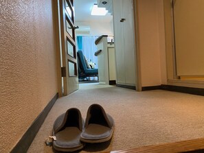 A hallway with a pair of slippers on the floor, a door leading to a room with a bed and a chair, and a wall-mounted air conditioning unit. - Today's Relaxing and Fun Studio! Near Olympic Park! (Setagaya)