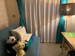 A room with a blue sofa, a small table, a lamp, and a panda plush toy.