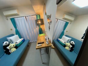 A compact room with two blue sofas, a wooden table, and an air conditioning unit on the wall.