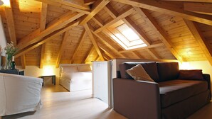 Une pièce mansardée chaleureuse avec des poutres en bois, un canapé, une petite table et une fenêtre.