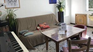 Een woonkamer met een bank, een tafel, een piano en diverse decoratieve objecten.