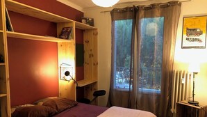 Een slaapkamer met een bed, bureau, stoel, plank, raam met gordijnen en een poster aan de muur.
