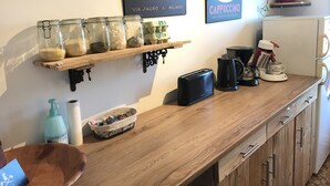 Een aanrecht met potten en kruiden, een broodrooster, een koffiezetapparaat en een plank met boeken.