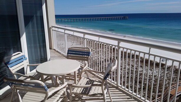 A balcony with a table and chairs, overlooking a beach with a pier. - Peral 605 Sugar White Sand and Emerald Waters! Beautiful Gulf Views!  (Navarre)