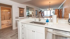 A modern kitchen with a large island, white cabinetry, and a stainless steel sink. - Peral 605 Sugar White Sand and Emerald Waters! Beautiful Gulf Views!  (Navarre)