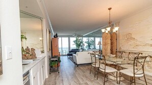 A spacious living area with a dining table and chairs, a sofa, and a view of the outdoors. - Peral 605 Sugar White Sand and Emerald Waters! Beautiful Gulf Views!  (Navarre)
