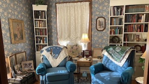 Une pièce chaleureuse avec deux fauteuils bleus, un tapis à motifs, une bibliothèque et un bureau avec une lampe.