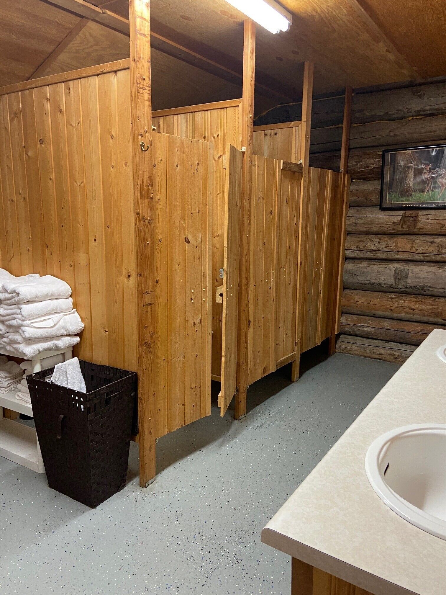 A wooden cabin bathroom with a sink, a stack of towels, and a trash bin.