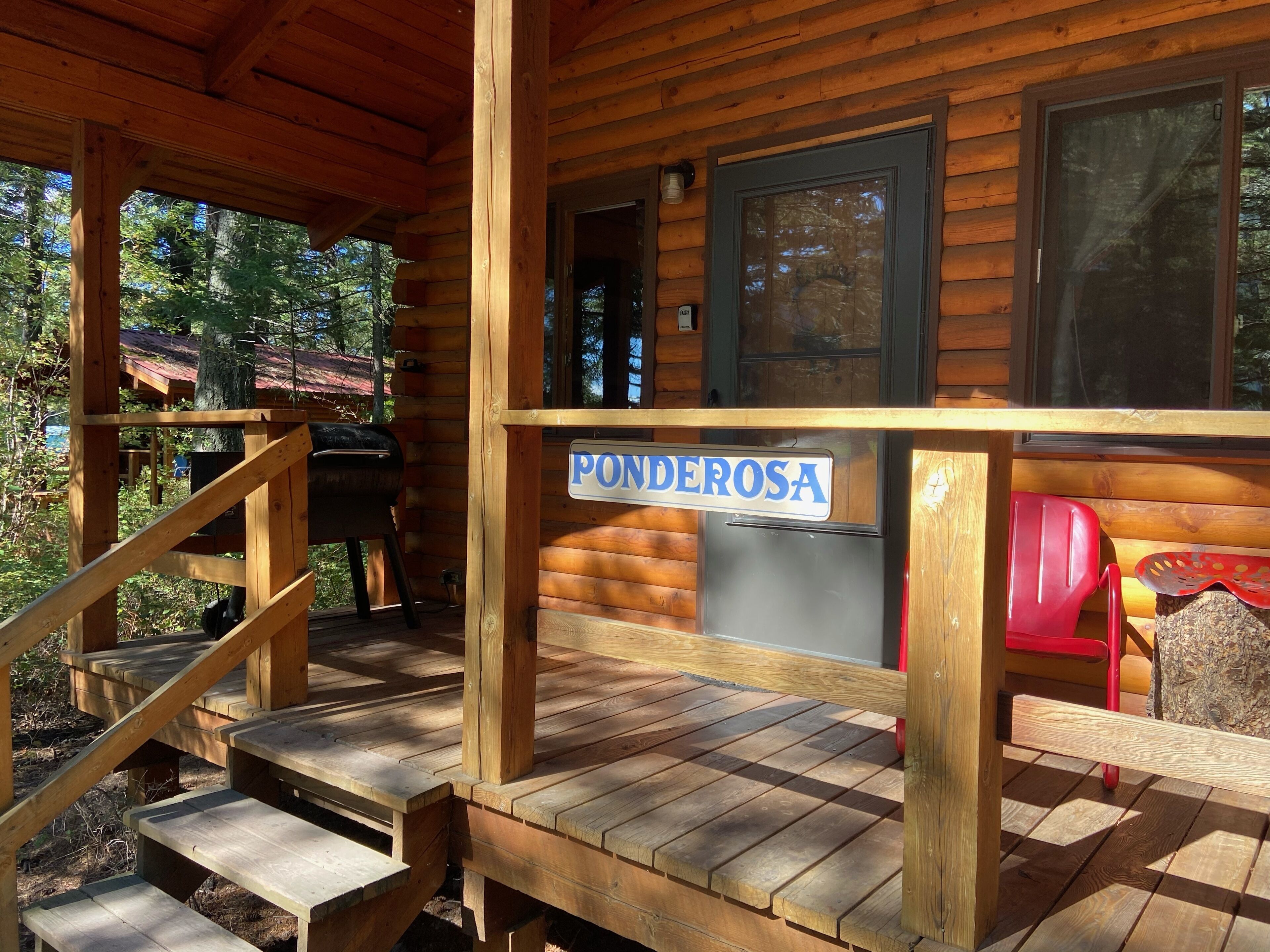 Eine Holzhütte mit Veranda, einem Schild mit der Aufschrift 'Ponderosa' und einem roten Stuhl.