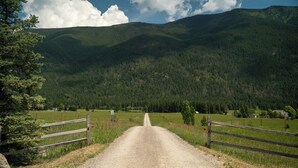 A rural road leading into a forested valley with a clear sky. - Ponderosa Cabin Columbia Mountain Ranch (Columbia Falls)