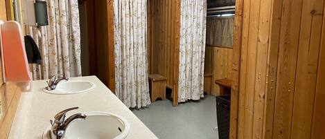 Un baño de cabaña de madera con dos lavabos, una cortina de ducha y un cubo de basura.