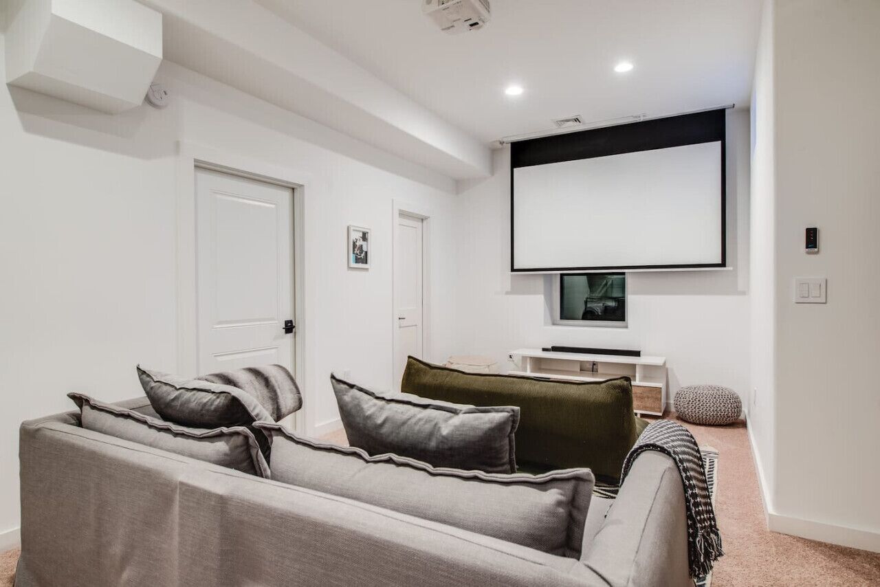 Ein modernes Wohnzimmer mit einem grauen Sofa, einem an der Wand befestigten Fernseher und einer weißen Decke.