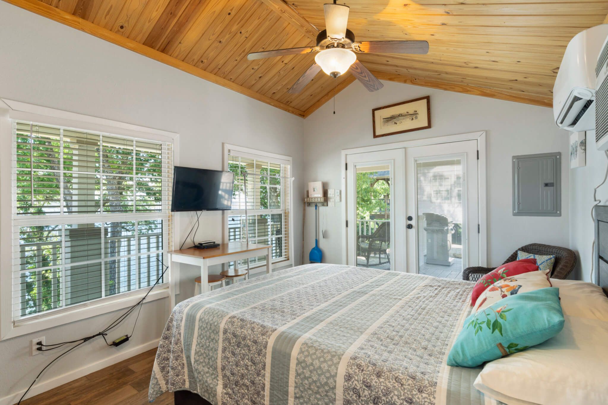 A bedroom with a bed, a ceiling fan, a TV, and a window with blinds.