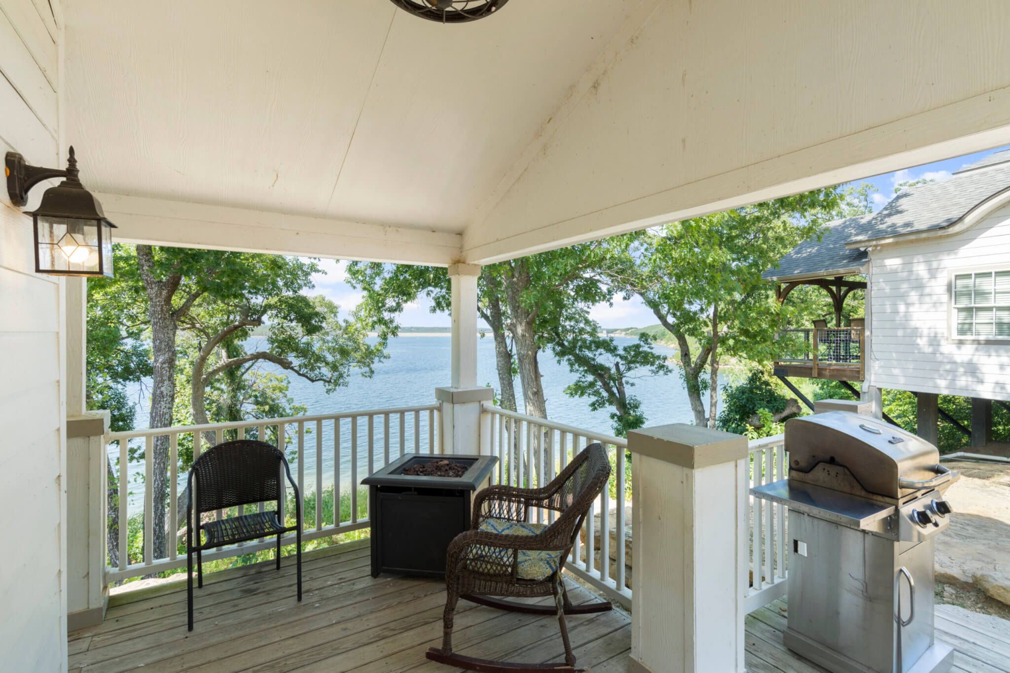 A covered porch with a grill, two wicker chairs, and a table.