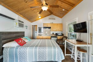 Une petite chambre comprenant un lit, un coin cuisine, un ventilateur de plafond et un téléviseur.