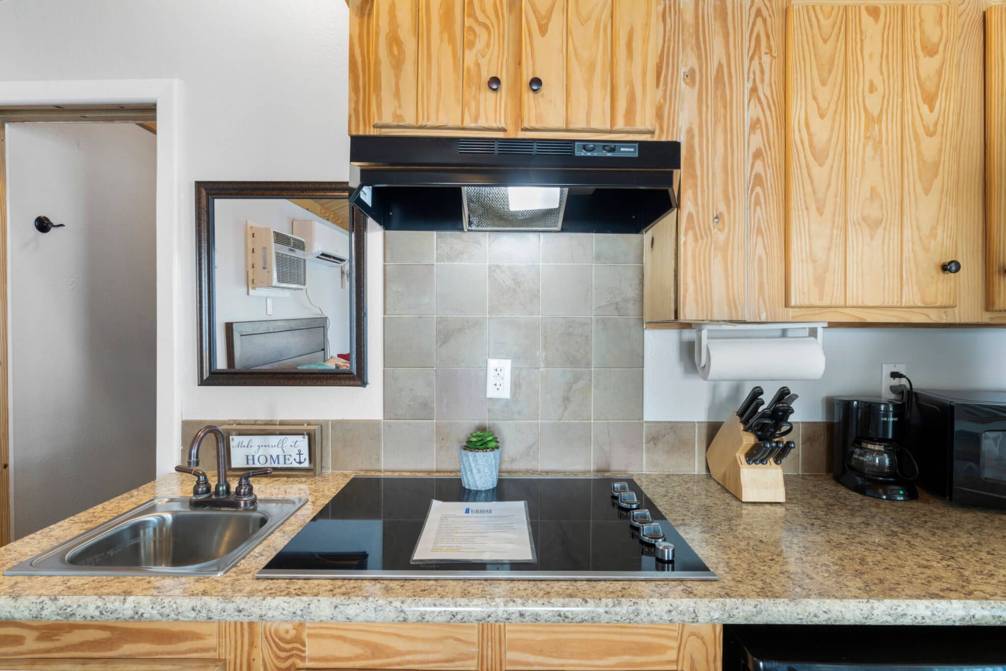 A kitchen with wooden cabinets, a stainless steel sink, a black stove, and a countertop with a knife block and a coffee maker.