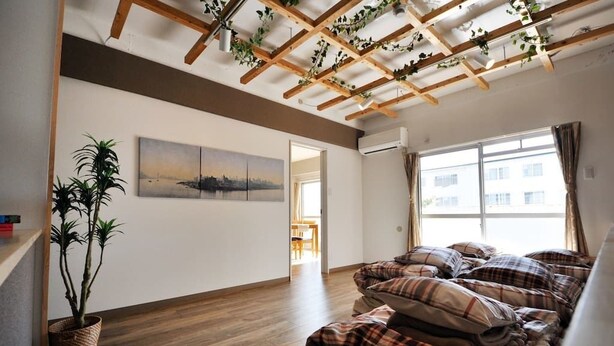 A room with a wooden ceiling, a large window, a bed with plaid bedding, a potted plant, and a painting on the wall. - Tarbo's House TDS Recently Renovated (Nara)