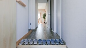 A hallway with a wooden floor and a series of shoes lined up on the steps. - Tarbo's House TDS Recently Renovated (Nara)