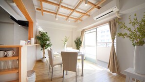 A modern dining area with a wooden ceiling, white walls, and a large window with curtains. There are potted plants and a white table with chairs. - Tarbo's House TDS Recently Renovated (Nara)