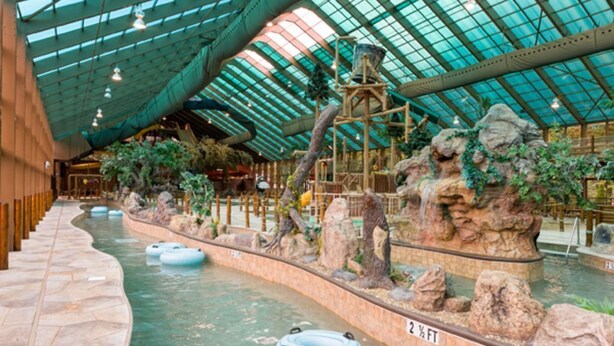 Un parc aquatique intérieur doté d’un toit en verre, de formations rocheuses artificielles et de bouées gonflables.