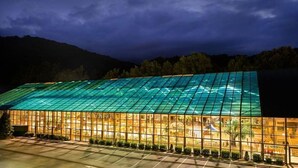 Un grand bâtiment doté d’une façade en verre et d’un toit végétalisé, entouré d’arbres et de collines.