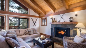 A cozy living room with a fireplace, a sofa, a coffee table, and a patterned armchair. - Newly Remodeled Luxurious Craftsman Home  (IVGID)