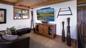 A living room with a wooden ceiling, a large flat-screen TV, a wooden cabinet, and two vases. - Newly Remodeled Luxurious Craftsman Home  (IVGID)