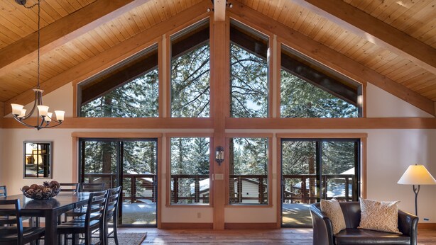 A spacious room with a high ceiling, large windows, a dining area, and a cozy seating area. - Newly Remodeled Luxurious Craftsman Home  (IVGID)