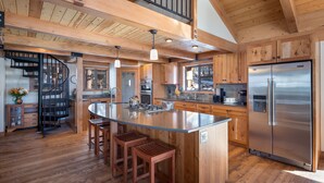 A spacious kitchen with a large island, wooden cabinets, stainless steel appliances, and a spiral staircase. - Newly Remodeled Luxurious Craftsman Home  (IVGID)