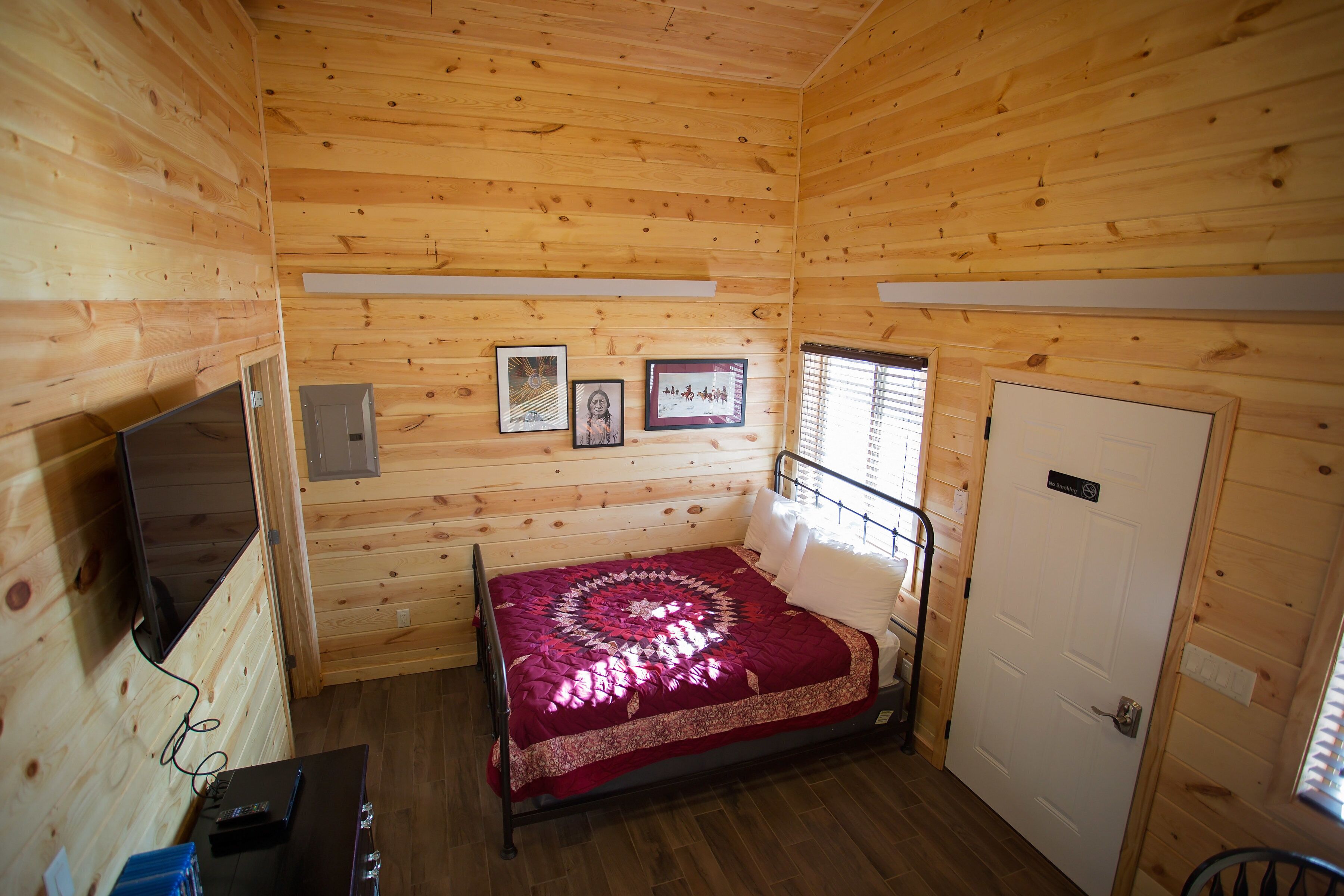 A wooden cabin room with a bed, a TV, and a door.