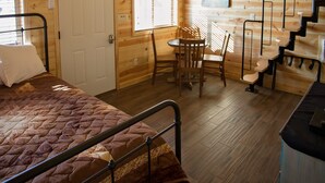 Interior de una cabaña de madera con una cama, una mesa de comedor y una escalera.
