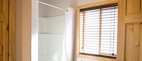Ein Badezimmer mit Duschkabine aus Glas, Holztüren, einem Fenster mit Rollo und einem Handtuchhalter.