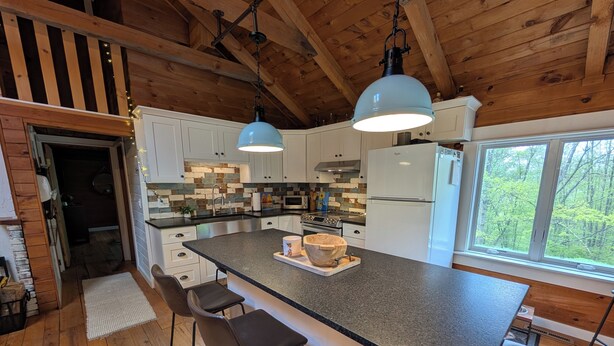 A modern kitchen with a large island, wooden cabinets, and pendant lighting.