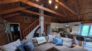 A cozy cabin interior with a large sectional sofa, a kitchen with modern appliances, and a wooden staircase.
