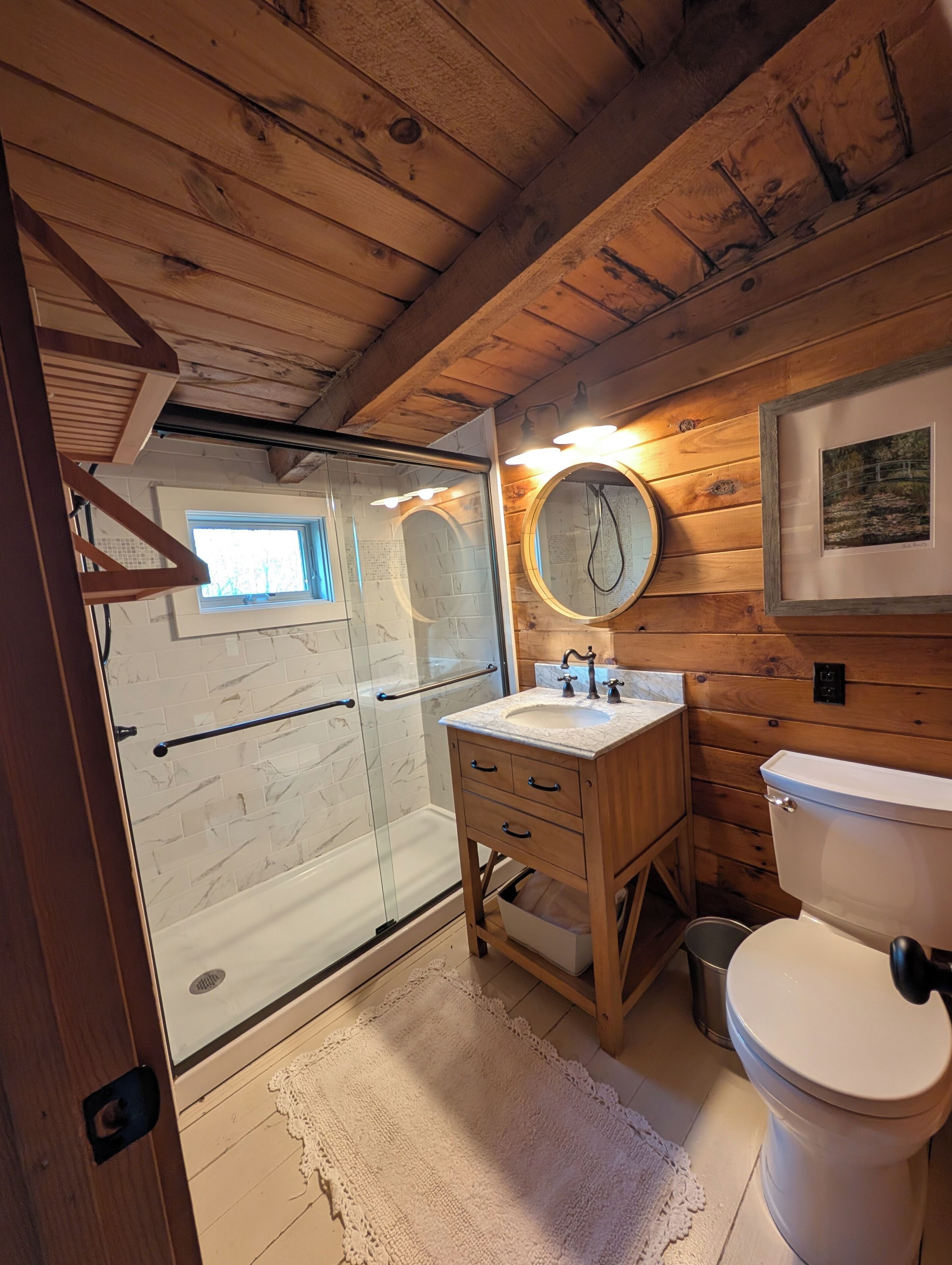 A bathroom with a glass shower enclosure, wooden vanity, and a white toilet.
