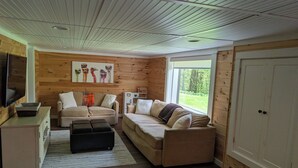 A cozy living room with a wooden ceiling, a large window, and a painting of colorful birds.
