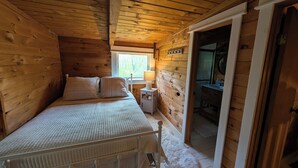 A wooden cabin bedroom with a bed, bedside table, and a view of the bathroom.